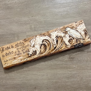 May include: A wooden plaque with a pyrography design of ocean waves and a bird. The text "He stifled the storm, the waves of the sea were hushed" is included. Psalm 107:29 is also written on the plaque.