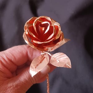 May include: A copper rose with two leaves, the rose is made of multiple layers of copper and has a reddish-brown color.