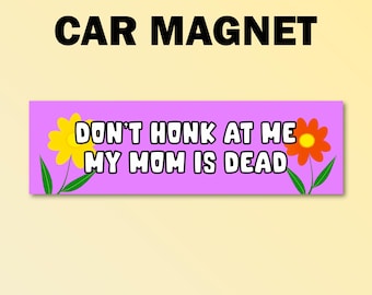 Könnte beinhalten: Ein rechteckiger Autoaufkleber mit dem Text "CAR MAGNET" oben. Darunter zeigt ein lila Rechteck den Text "DON'T HONK AT ME MY MOM IS DEAD" mit einer gelben und einer orangefarbenen Blume auf jeder Seite.