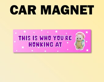 Könnte beinhalten: Ein Auto-Magnet mit dem Text "CAR MAGNET" in Schwarz. Darunter befindet sich ein rosa Rechteck mit dem Text "THIS IS WHO YOU'RE HONKING AT" in Lila, mit einer Cartoon-Katzen-Illustration.