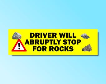 May include: Yellow warning sign with black text that reads "DRIVER WILL ABRUPTLY STOP FOR ROCKS". The sign has a red exclamation point inside a triangle and three gray rocks on the top and bottom.