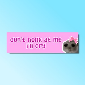 以下が含まれることがあります： ピンクと白のステッカーに「don't honk at me i'll cry」というテキストと、ピンクのリボンをした猫の漫画の画像が描かれています。