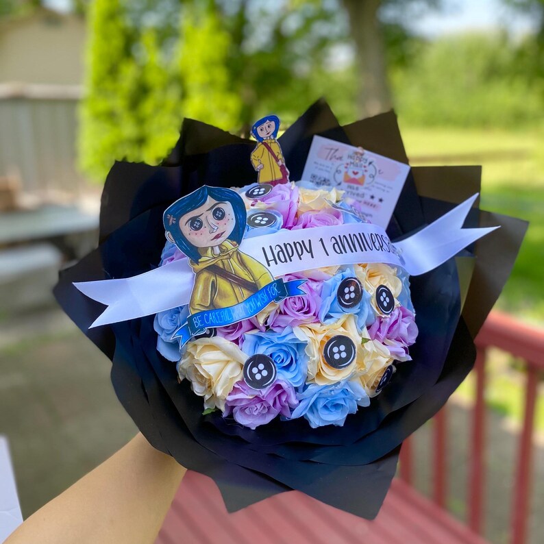 Puede incluir: Un ramo de rosas de color pastel con adornos de botones, con un personaje de la pel&iacute;cula "Coraline" y una cinta que dice "Feliz 1 aniversario".