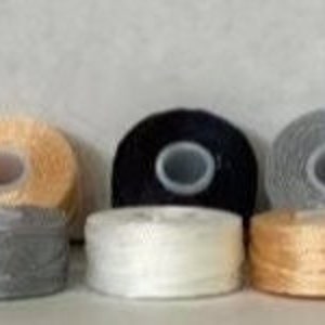 May include: Six spools of embroidery floss in various colors, including beige, black, gray, white, and gold.