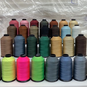 May include: A collection of 30 spools of thread in various colors, including green, blue, brown, pink, and gray. The spools are arranged in a triangular shape on a white surface.