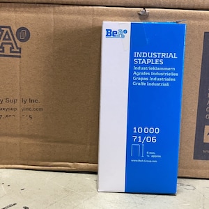 May include: A box of industrial staples with a blue and white label. The label reads "INDUSTRIAL STAPLES" in multiple languages and includes the quantity "10000 71/06". The box is next to a brown cardboard box with the "BeA" logo.