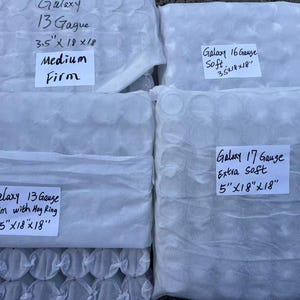 May include: Four white packages containing mattress innerspring coils. The packages are labeled with the brand name "Galaxy" and the gauge, size, and firmness of the innerspring coils. The labels read: "Galaxy 13 Gauge 3.5"x18"x18" Medium Firm", "Galaxy 16 Gauge Soft 3.5"x18"x18"", "Galaxy 13 Gauge Firm with Hoy Ring 3.5"x18"x18"", and "Galaxy 17 Gauge Extra Soft 5"x18"x18"".