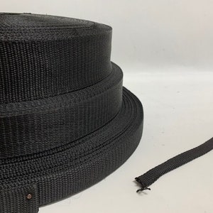 May include: A roll of black nylon webbing, a type of strong, durable fabric often used for straps, belts, and other applications.