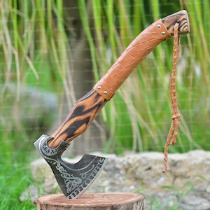 Pode incluir: Um machado viking forjado à mão com um cabo de madeira preto e marrom, um envoltório de couro e um cordão de couro. A cabeça do machado é gravada com um símbolo viking e a palavra "ÖVERKRAFT".