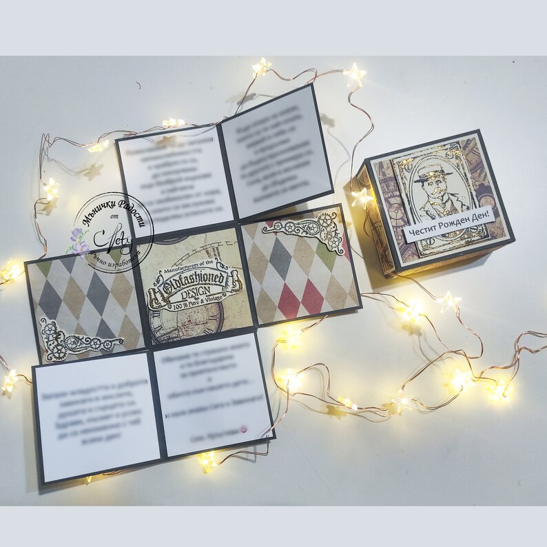 May include: A brown and gold explosion box with a vintage design. The box is decorated with a compass, gears, and a checkered pattern. The box is open and has a message inside that says "Happy Birthday".