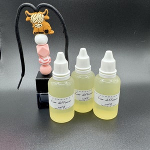May include: Three clear glass bottles with white caps and labels that say "Car diffuser refill Musk Stick" and a black bottle with a white cap and a label that says "Candles Car diffuser refill Musk Stick". There is a black cord with a pink, white, and brown cow charm attached.