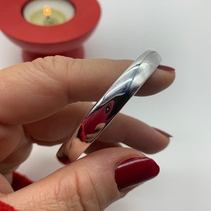 May include: A shiny silver bangle bracelet with a smooth, rounded surface.