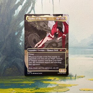 May include: A Magic: The Gathering trading card titled Kaalia of the Vast, featuring a legendary human cleric with red wings, a dark hooded cloak, and a large dragon. The card displays game text, mana symbols, and a power and toughness of 2/2.