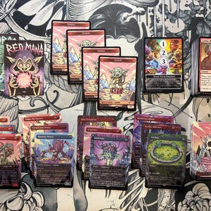 May include: A collection of Magic: The Gathering trading cards featuring various illustrations and text. The cards display a range of colors, including red, pink, green, and purple, with fantasy-themed artwork. Some cards have the word "Goblin" on them.