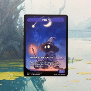 May include: A rectangular trading card featuring a dark-robed wizard character with a pointed hat holding a glowing staff. The background is a starry night sky with a crescent moon. Text includes Wizard, Token Creature, and game rules.