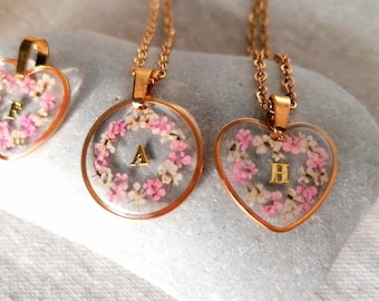May include: Three gold necklaces with different pendants. The pendants are made of clear resin with dried pink flowers and a gold letter inside. The letters are A, H, and F.