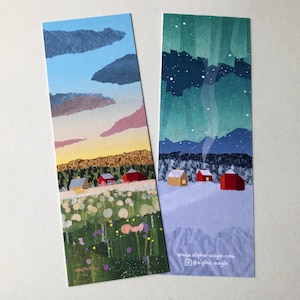 May include: Two landscape-themed bookmarks. One shows a sunset over a village with red houses and a field of flowers. The other depicts a snowy village under a starry night sky with the text "alpha angle".