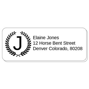 May include: A rectangular white label with rounded corners. The label features a black laurel wreath surrounding the letter "J". Text on the label reads "Elaine Jones" and an address.