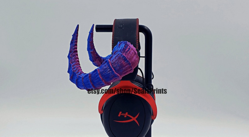 Pu&ograve; includere: Un paio di corna stampate in 3D blu e viola attaccate a un auricolare nero con accenti rossi. L'auricolare &egrave; su un supporto. Il testo "etsy.com/shop/SealPrints" &egrave; visibile sull'auricolare.