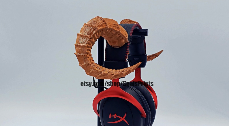 Pu&ograve; includere: Un paio di corna marroni stampate in 3D attaccate a un auricolare da gioco rosso. Le corna sono progettate per assomigliare a corna di drago. L'auricolare &egrave; su un supporto. etsy.com/shop/SealsPrints