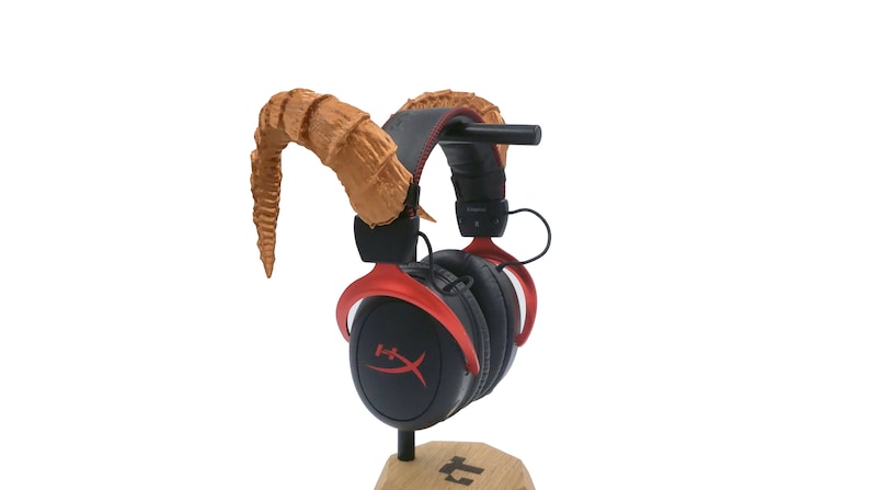 Pu&ograve; includere: Auricolare da gioco rosso e nero con corna marroni attaccate alla fascia. L'auricolare &egrave; su un supporto in legno.