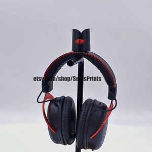 May include: Black headphones with red accents on a stand. The headphones have a black headband with red stitching and black earcups with red accents.