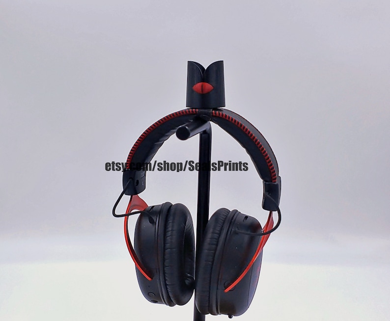 May include: Black headphones with red accents on a stand. The headphones have a black headband with red stitching and black earcups with red accents.