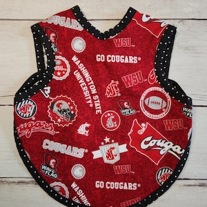 May include: A red baby bib with a black polka dot trim. The bib features Washington State University logos, text, and imagery, including the words "GO COUGARS" and "WASHINGTON STATE UNIVERSITY".