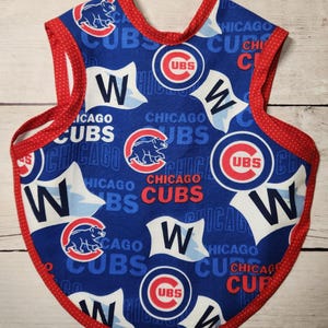 May include: Blue baby bib featuring the Chicago Cubs logo and team name in red and white. The bib has a red polka dot trim and straps. The design includes the Cubs bear logo and the letter "W".
