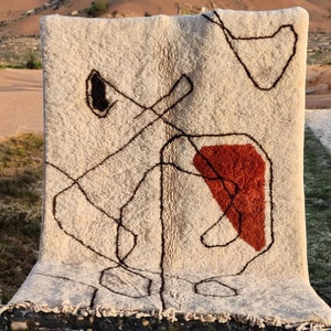 以下が含まれることがあります： 茶色とオレンジ色の抽象的なデザインが施された白い敷物。敷物はフリンジの縁取りがあり、ウール製です。