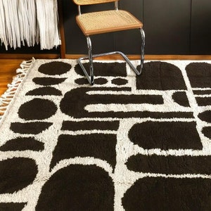 May include: A black and white geometric rug with a brown woven chair in the background.