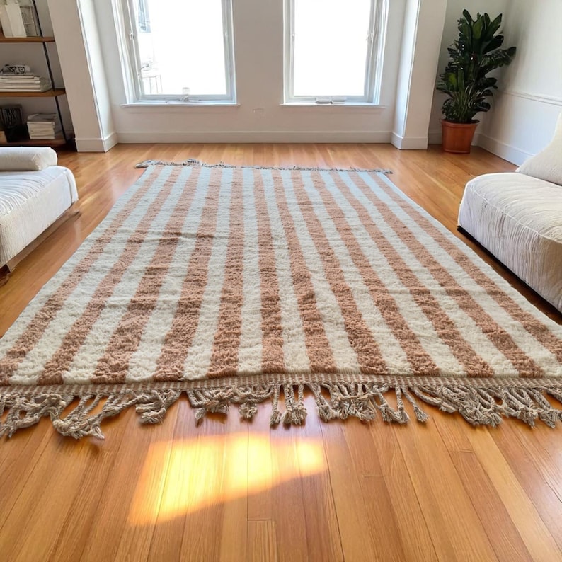Elegant handwoven Moroccan rug with vertical stripes in Cameo Rose and soft white. Perfect for boho, coastal, minimalist, or Japandi-inspired spaces. Made from natural wool, this artisan piece blends texture and comfort for your living room, bedroom, or entryway. A modern pastel rug with warm earthy tones and timeless Amazigh character. Custom sizes available.