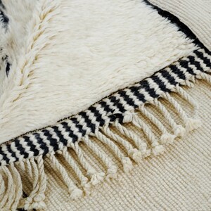 Handmade Moroccan wool rug featuring a minimalist black and white design. Ethically crafted by Berber artisans in Morocco using 100% natural wool. Thick, plush, and ultra-soft, this Beni Ourain-style carpet is perfect for modern, Scandinavian, and bohemian interiors. Ideal for living rooms, bedrooms, and luxury home decor. Available in custom sizes. Authentic tribal craftsmanship with eco-friendly materials. Free worldwide shipping with FedEx Express.