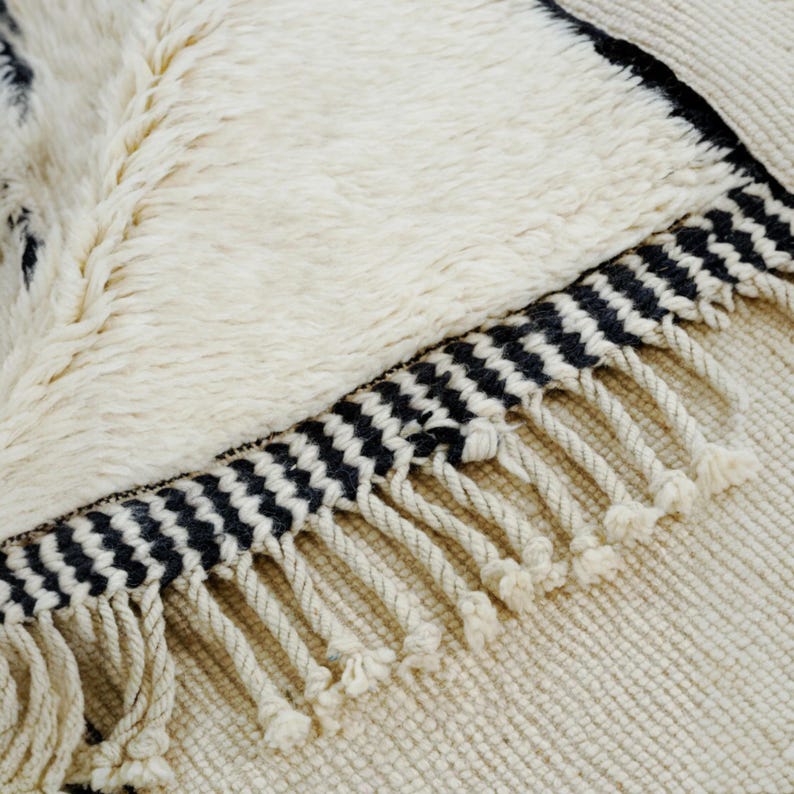 Handmade Moroccan wool rug featuring a minimalist black and white design. Ethically crafted by Berber artisans in Morocco using 100% natural wool. Thick, plush, and ultra-soft, this Beni Ourain-style carpet is perfect for modern, Scandinavian, and bohemian interiors. Ideal for living rooms, bedrooms, and luxury home decor. Available in custom sizes. Authentic tribal craftsmanship with eco-friendly materials. Free worldwide shipping with FedEx Express.