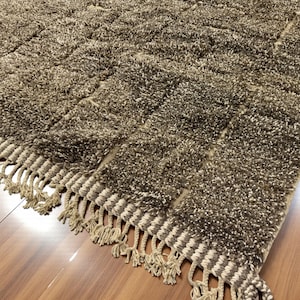 Handwoven Moroccan rug made from 100% natural wool in Travertine and White tones. Its rich texture and neutral color palette make it the perfect statement piece for modern, minimalist, or boho interiors. Crafted by Amazigh artisans in the Atlas Mountains, this rug combines traditional Moroccan weaving with a soft, earthy design. Ideal for living rooms, bedrooms, or cozy reading spaces, it brings warmth and timeless elegance to your home.