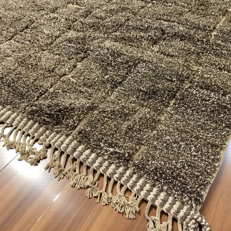 Handwoven Moroccan rug made from 100% natural wool in Travertine and White tones. Its rich texture and neutral color palette make it the perfect statement piece for modern, minimalist, or boho interiors. Crafted by Amazigh artisans in the Atlas Mountains, this rug combines traditional Moroccan weaving with a soft, earthy design. Ideal for living rooms, bedrooms, or cozy reading spaces, it brings warmth and timeless elegance to your home.