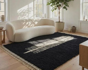 May include: A rectangular area rug featuring a deep black, textured pile with a central white geometric grid pattern and long, cream-coloured fringe along the shorter edges. The rug is crafted with a thick, shaggy weave and sits flat.