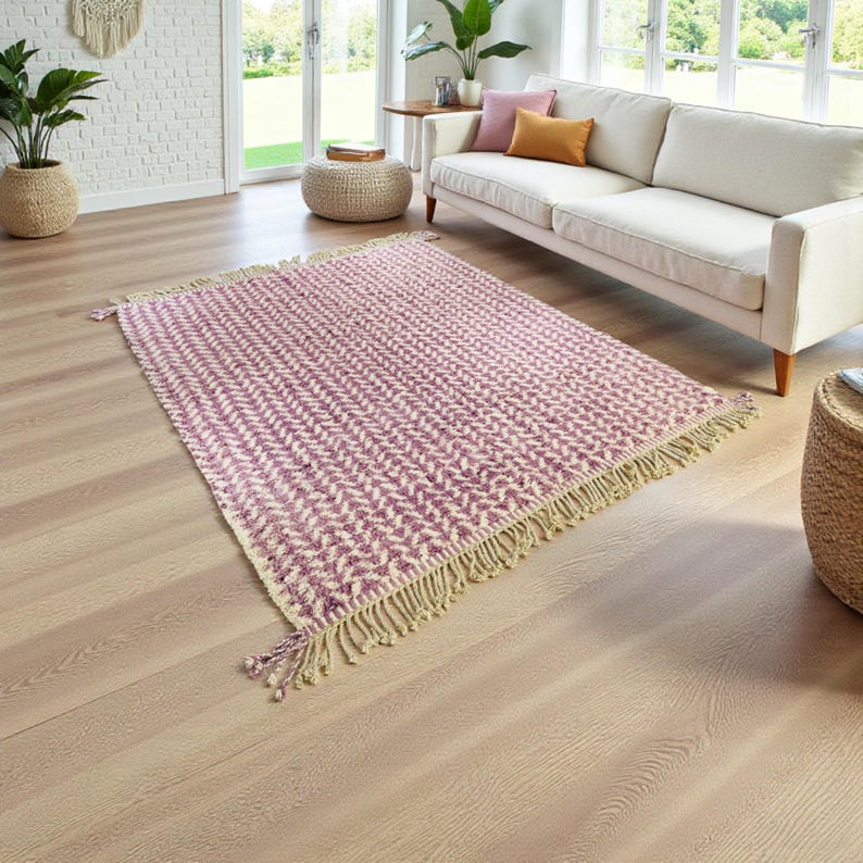 Handwoven Moroccan wool rug in wistful mauve and cream tones. Features a soft geometric pattern with textured pile and hand-knotted fringes. Perfect for living rooms, bedrooms, or boho interiors. Made from 100% natural wool by Berber artisans in Morocco. This handmade rug adds warmth, elegance, and Moroccan authenticity to modern or vintage-style spaces.