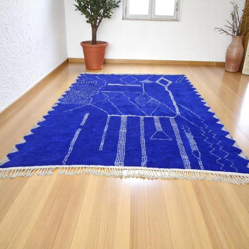 Striking handmade Moroccan rug in bold cobalt blue with white tribal Amazigh symbols. Crafted from natural wool, this unique Berber rug features traditional abstract lines and diamond motifs, perfect for adding a splash of color and culture to modern interiors. Ideal for boho, eclectic, or contemporary homes looking for a statement piece. Soft texture and timeless authenticity.
