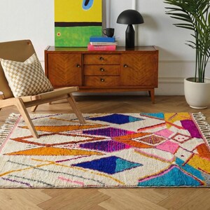 Authentic handmade Moroccan Boujaad rug featuring bold geometric diamond patterns in vibrant multicolor — electric blue, fuchsia pink, orange, yellow and purple on ivory wool background. Hand-knotted by Berber artisans in Morocco using natural wool. Perfect boho statement rug for living room, bedroom or dining room. One-of-a-kind colorful area rug with traditional fringe.