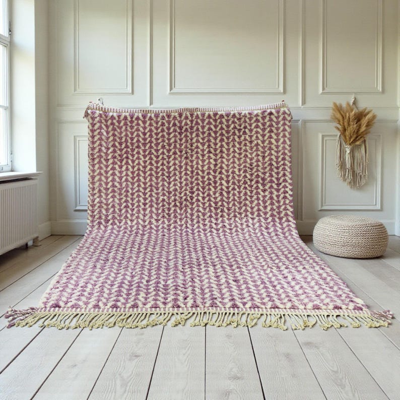 Handwoven Moroccan wool rug in wistful mauve and cream tones. Features a soft geometric pattern with textured pile and hand-knotted fringes. Perfect for living rooms, bedrooms, or boho interiors. Made from 100% natural wool by Berber artisans in Morocco. This handmade rug adds warmth, elegance, and Moroccan authenticity to modern or vintage-style spaces.
