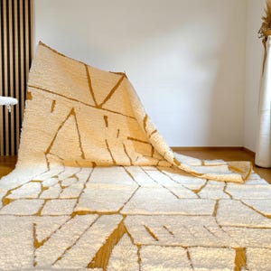 Handmade Moroccan rug in a soft ivory base with striking mustard yellow (Thai Curry) abstract lines. Woven by Berber artisans in pure wool, this rug blends tradition and modern style. Its geometric tribal pattern and warm tones make it perfect for living rooms, bedrooms, or creative interiors. Durable, eco-friendly, and soft underfoot, this ivory and mustard Berber carpet adds Moroccan charm and luxury to boho, modern, or eclectic home decor.