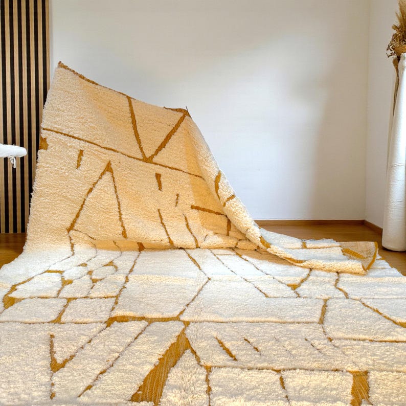 Handmade Moroccan rug in a soft ivory base with striking mustard yellow (Thai Curry) abstract lines. Woven by Berber artisans in pure wool, this rug blends tradition and modern style. Its geometric tribal pattern and warm tones make it perfect for living rooms, bedrooms, or creative interiors. Durable, eco-friendly, and soft underfoot, this ivory and mustard Berber carpet adds Moroccan charm and luxury to boho, modern, or eclectic home decor.