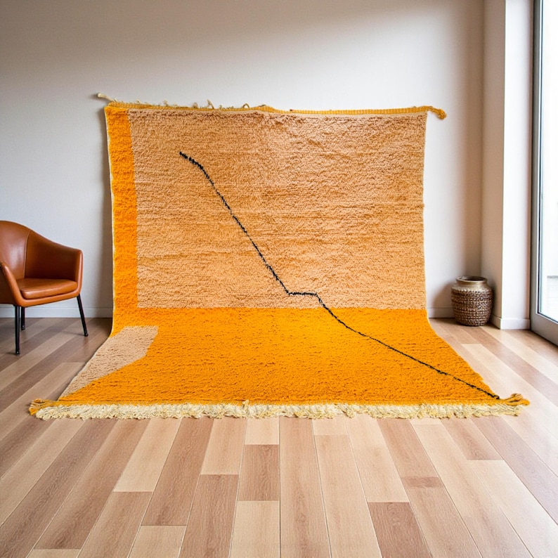 Handmade Moroccan rug in vibrant orange and soft beige with a bold abstract line design. Crafted by Berber artisans using pure wool, this rug combines traditional weaving with a modern artistic touch. Its warm, energetic tones make it a standout for living rooms, creative interiors, or bohemian spaces. Durable, eco-friendly, and soft underfoot, this orange and beige Berber wool carpet adds Moroccan charm and contemporary elegance to any home decor.