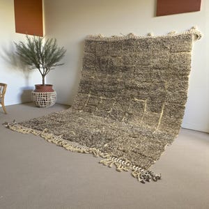 Handwoven Moroccan rug made from 100% natural wool in Travertine and White tones. Its rich texture and neutral color palette make it the perfect statement piece for modern, minimalist, or boho interiors. Crafted by Amazigh artisans in the Atlas Mountains, this rug combines traditional Moroccan weaving with a soft, earthy design. Ideal for living rooms, bedrooms, or cozy reading spaces, it brings warmth and timeless elegance to your home.