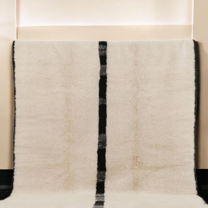 Handmade Moroccan wool rug featuring a minimalist black and white design. Ethically crafted by Berber artisans in Morocco using 100% natural wool. Thick, plush, and ultra-soft, this Beni Ourain-style carpet is perfect for modern, Scandinavian, and bohemian interiors. Ideal for living rooms, bedrooms, and luxury home decor. Available in custom sizes. Authentic tribal craftsmanship with eco-friendly materials. Free worldwide shipping with FedEx Express.