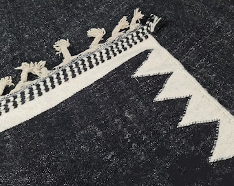 May include: Black and white rug with a geometric pattern and fringe. The rug has a black background with white geometric shapes and a white fringe around the edges.