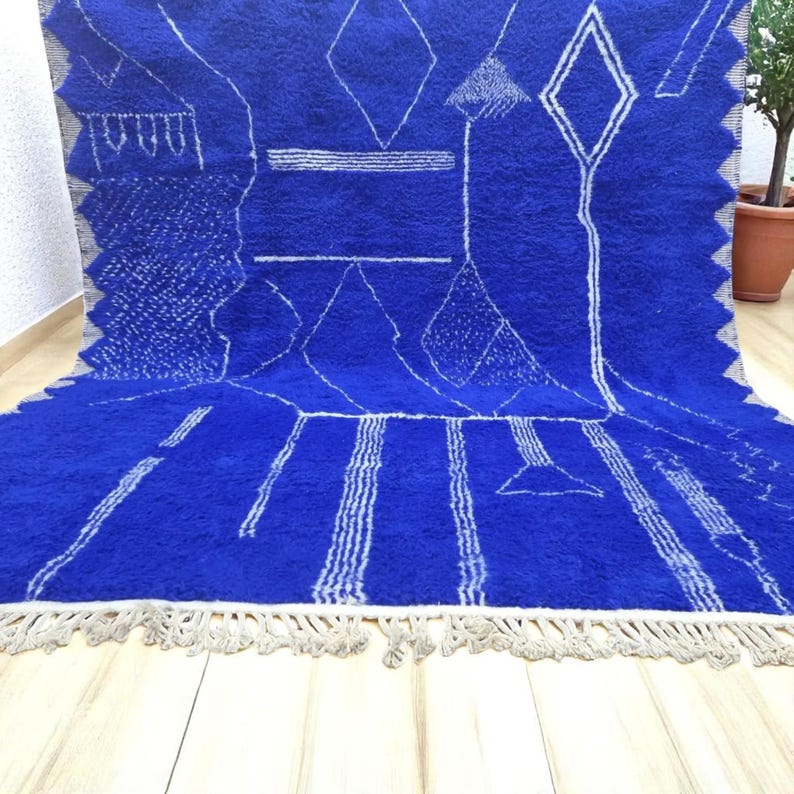 Striking handmade Moroccan rug in bold cobalt blue with white tribal Amazigh symbols. Crafted from natural wool, this unique Berber rug features traditional abstract lines and diamond motifs, perfect for adding a splash of color and culture to modern interiors. Ideal for boho, eclectic, or contemporary homes looking for a statement piece. Soft texture and timeless authenticity.