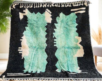 May include: A black and white rug with a large, abstract design in shades of teal and white. The rug has a fringe border.
