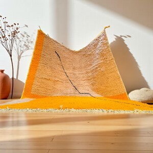 Handmade Moroccan rug in vibrant orange and soft beige with a bold abstract line design. Crafted by Berber artisans using pure wool, this rug combines traditional weaving with a modern artistic touch. Its warm, energetic tones make it a standout for living rooms, creative interiors, or bohemian spaces. Durable, eco-friendly, and soft underfoot, this orange and beige Berber wool carpet adds Moroccan charm and contemporary elegance to any home decor.